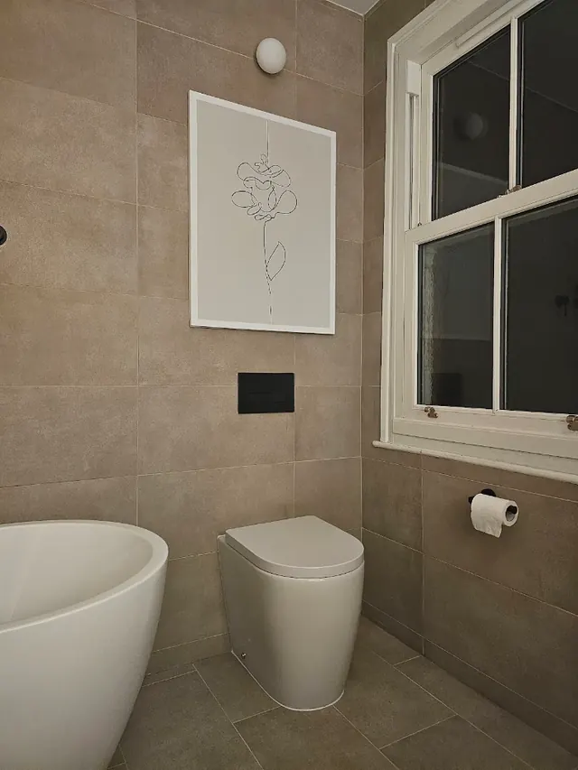 Back-to-wall toilet with a matt black flush plate, next to a freestanding bath