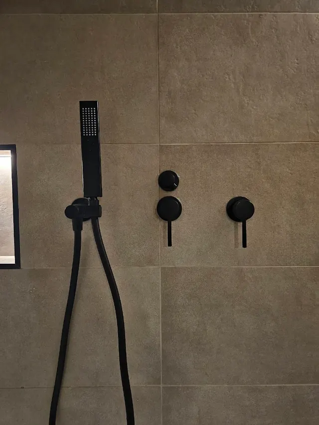 Concealed shower valves and hand shower in matt black, with a tiled niche alongside