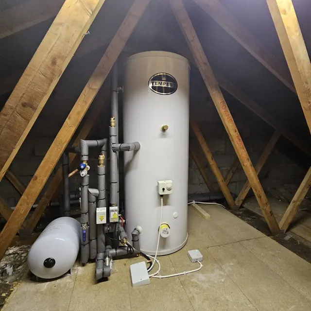 Unvented hot water cylinder fitted in a loft, with its expansion vessel and controls